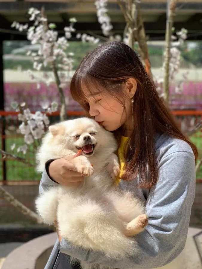 Một bạn trẻ đang bế chú chó nhỏ trên tay với nụ cười rạng rỡ giữa không gian xanh mướt của quán